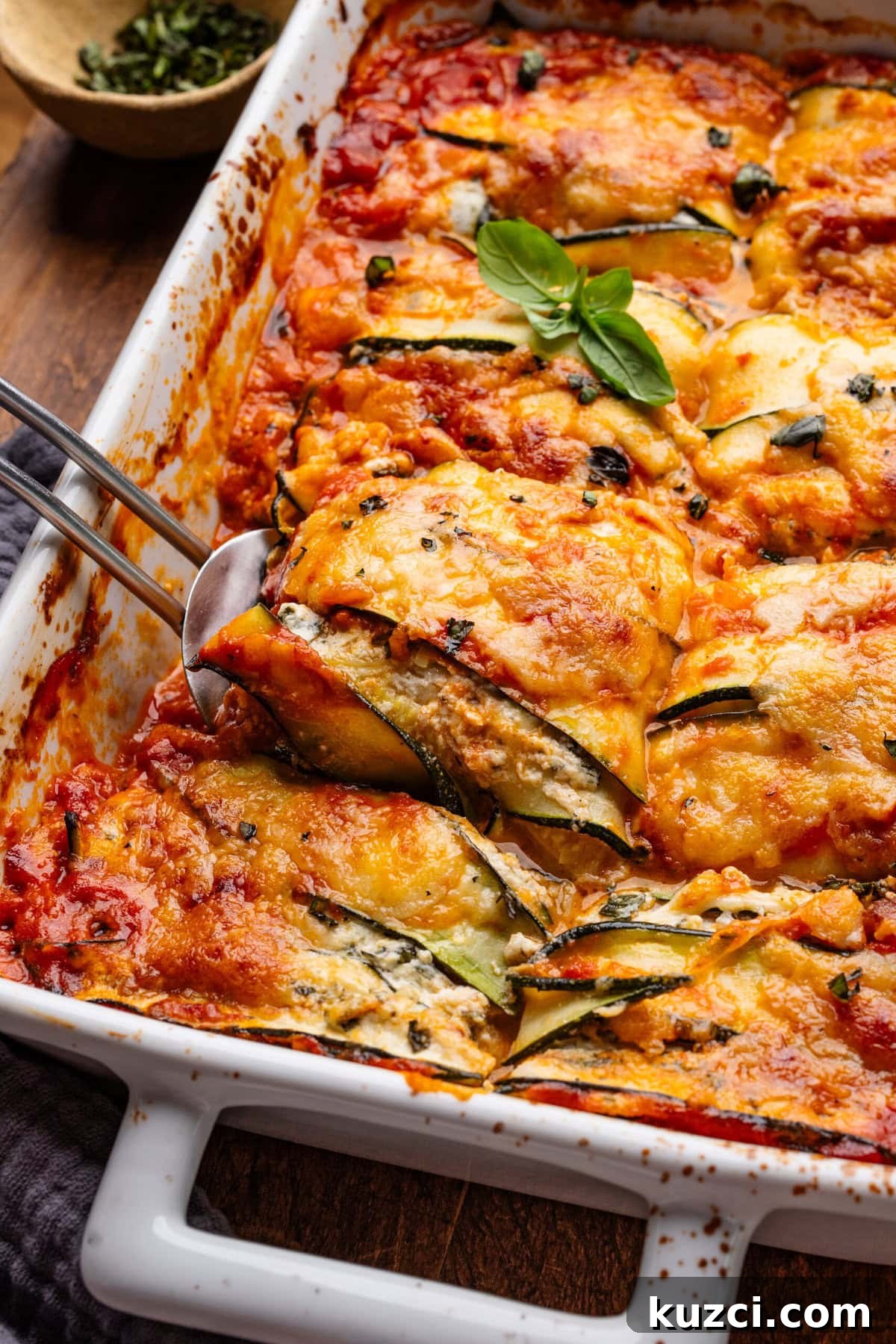 Zucchini Lasagna Recipe with Ricotta and Fresh Basil 8 A white baking dish with zucchini lasagna in it, a slice of the zucchini lasagna is being lifted out of the dish with a spatula.