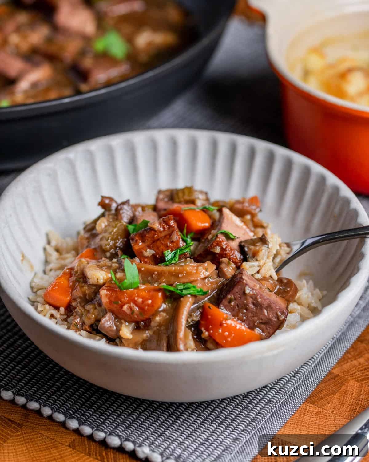 Vegan Stew with Smoked Tofu and Vegetables 6 Photo of a bowl of vegan stew over brown rice, set on a table mat with vegan cauliflower cheese in the background and the pan of stew.