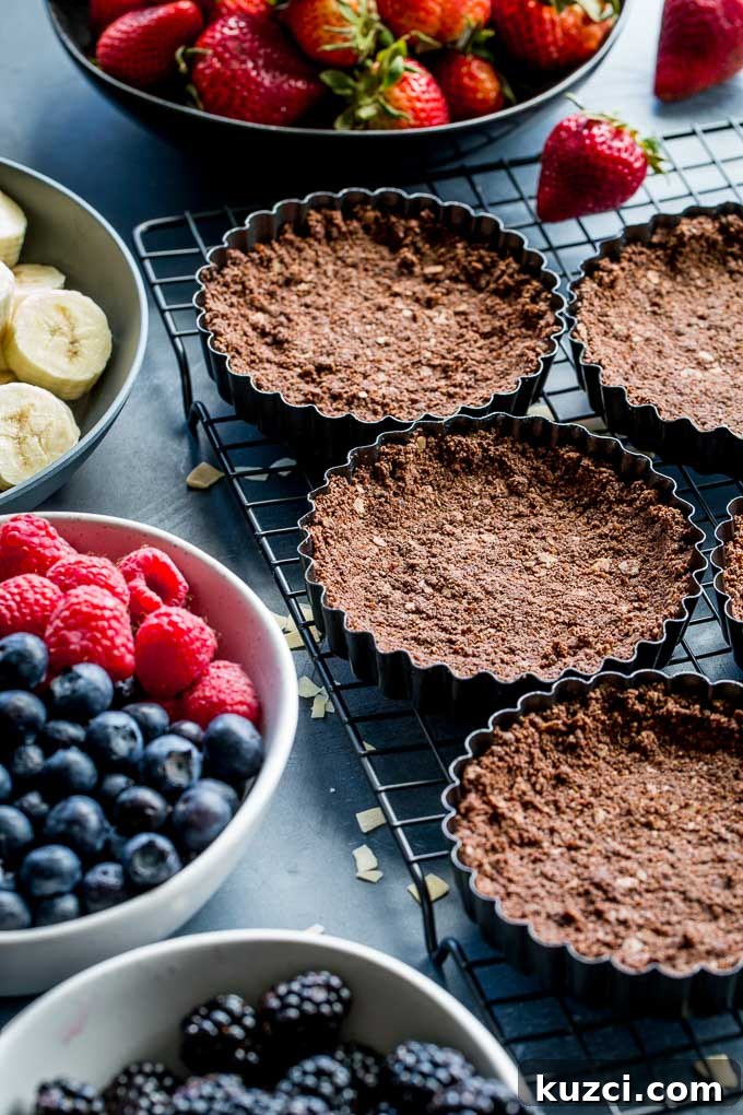 Chocolate tart shells cooling on a wire rack, next to bowls of fruit.