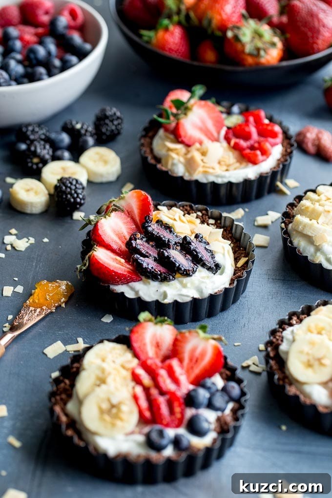 Mini fruit tarts arranged on a dark surface next to bowls of berries.