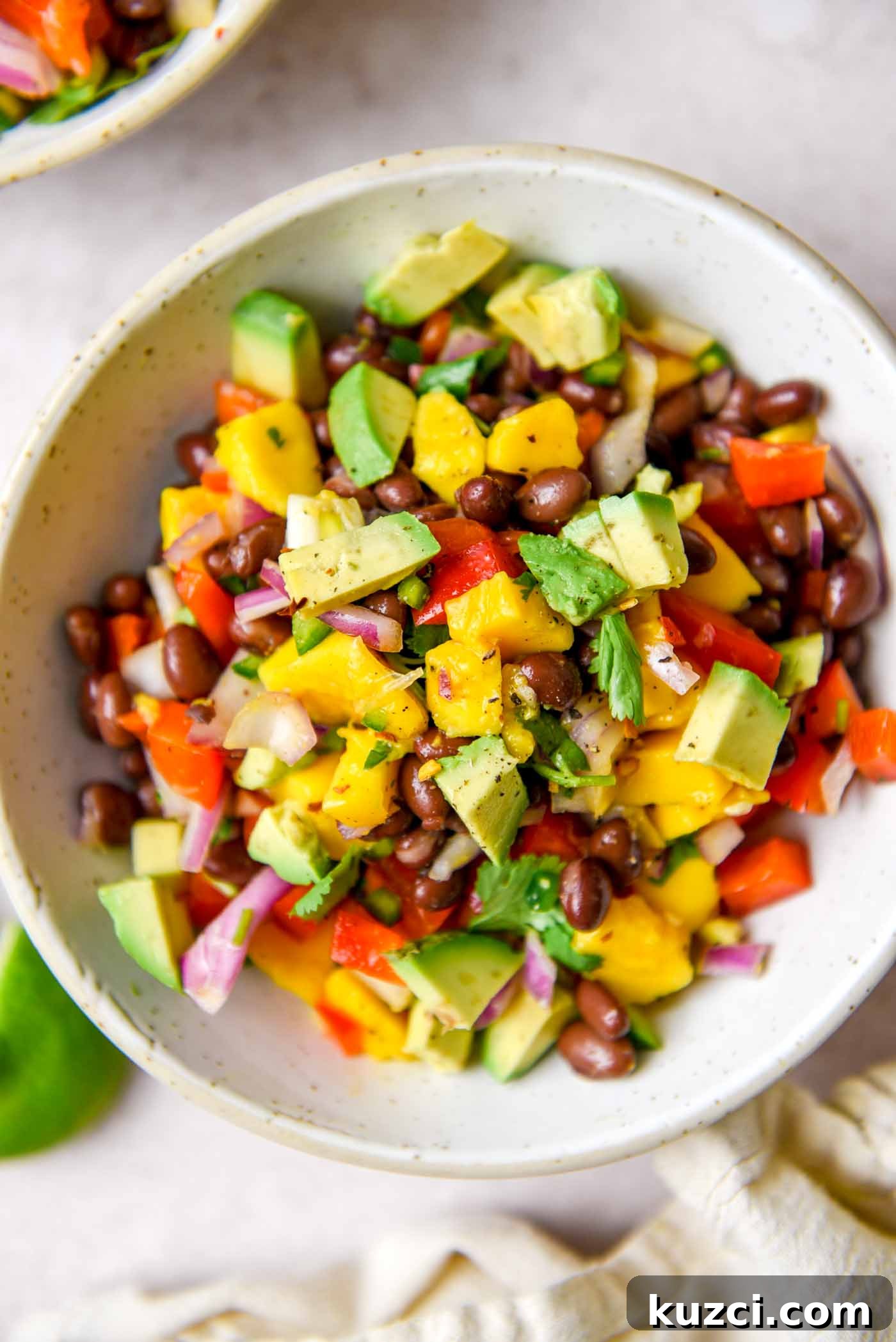 Bowl of mango and black bean salad with avocado, red bell pepper, red onion and cilantro.