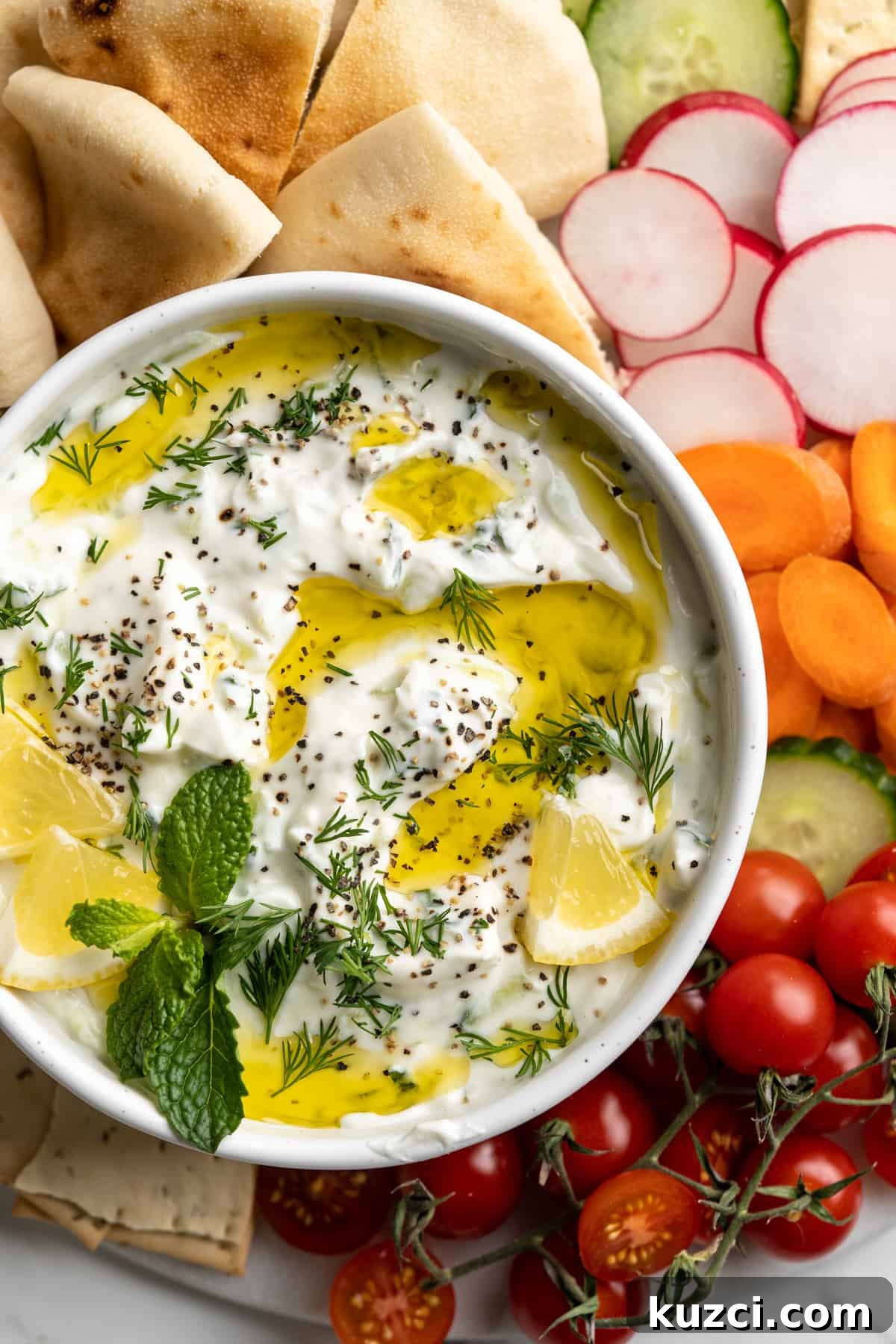 Tzatziki: Greek Yogurt and Cucumber Sauce Recipe 4 Overhead view of vegan tzatziki in bowl with drizzle of olive oil, fresh herbs, and lemon pieces