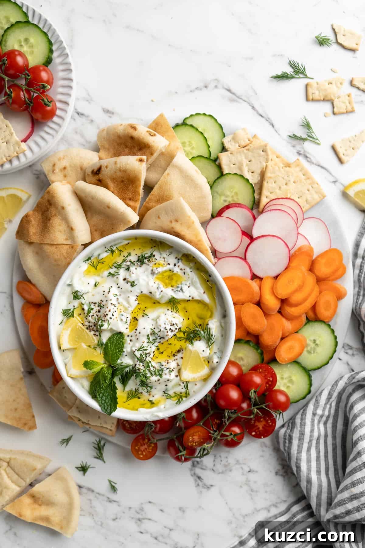 Tzatziki: Greek Yogurt and Cucumber Sauce Recipe 9 Overhead view of tzatziki in bowl on platter with vegetables, pita, and crackers