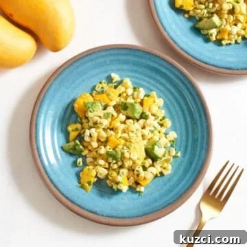 Two blue plates with mango corn salad on them, a gold fork is on the right, two mangoes are in the upper left.