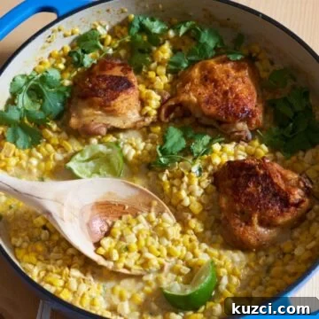 Chicken thighs with coconut milk and corn topped with fresh cilantro and lime wedges in a blue dish with a wooden spoon in it.