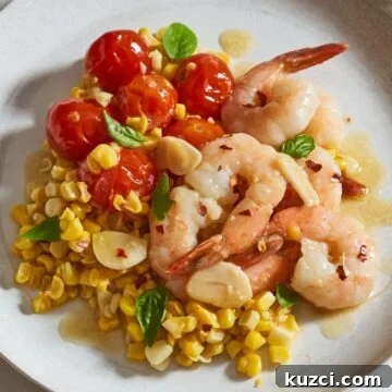 Shrimp scampi served over tomatoes and corn, topped with fresh basil on a white plate.