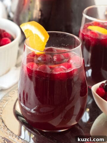 Two glasses of cranberry sangria with orange on a metal tray. White bowls with cranberries.