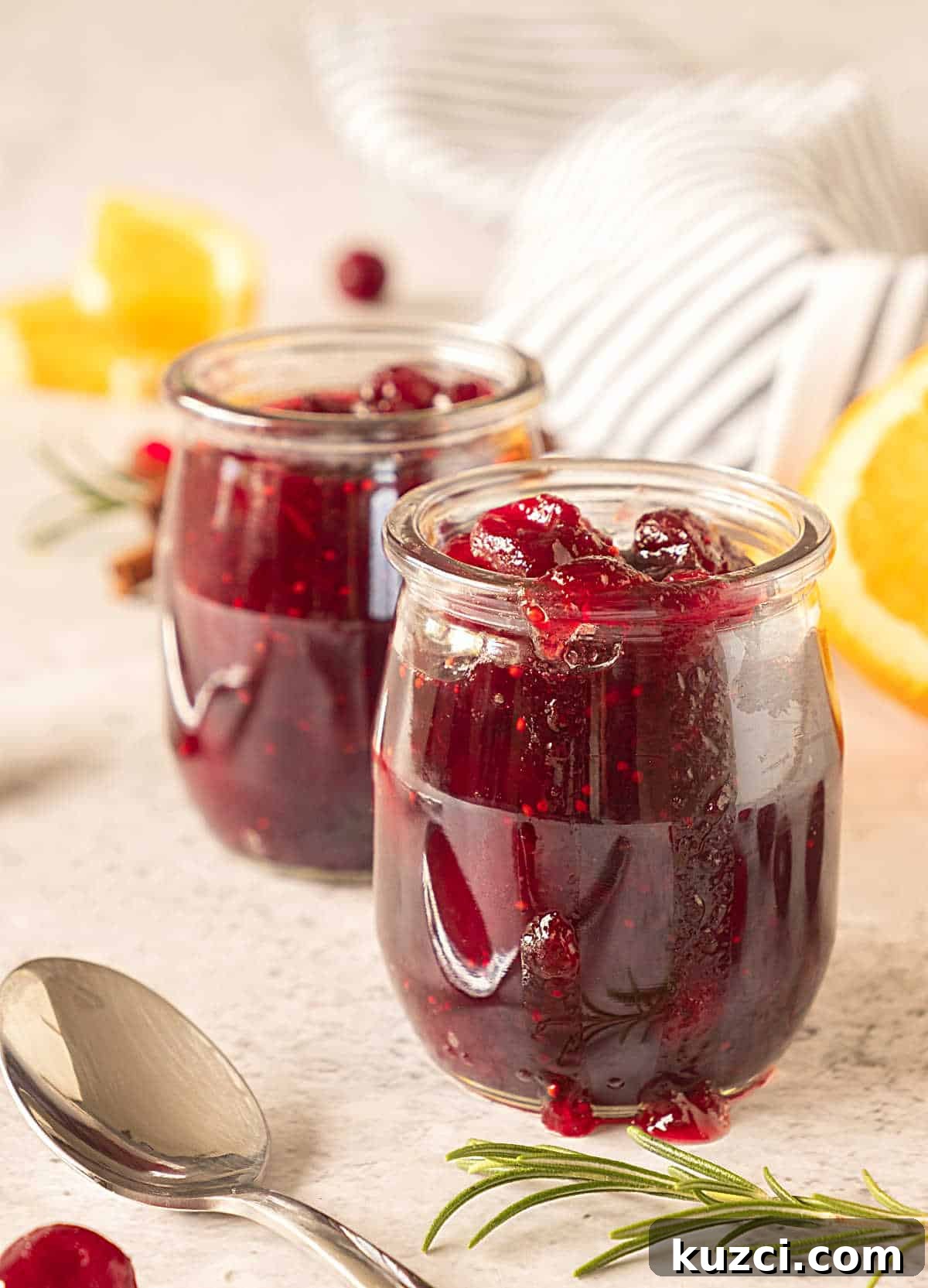 Homemade Cranberry Orange Sauce with Fresh Orange Juice 3 Two glass jars with cranberry sauce on a beige background with a striped cloth. Orange slices, a spoon.