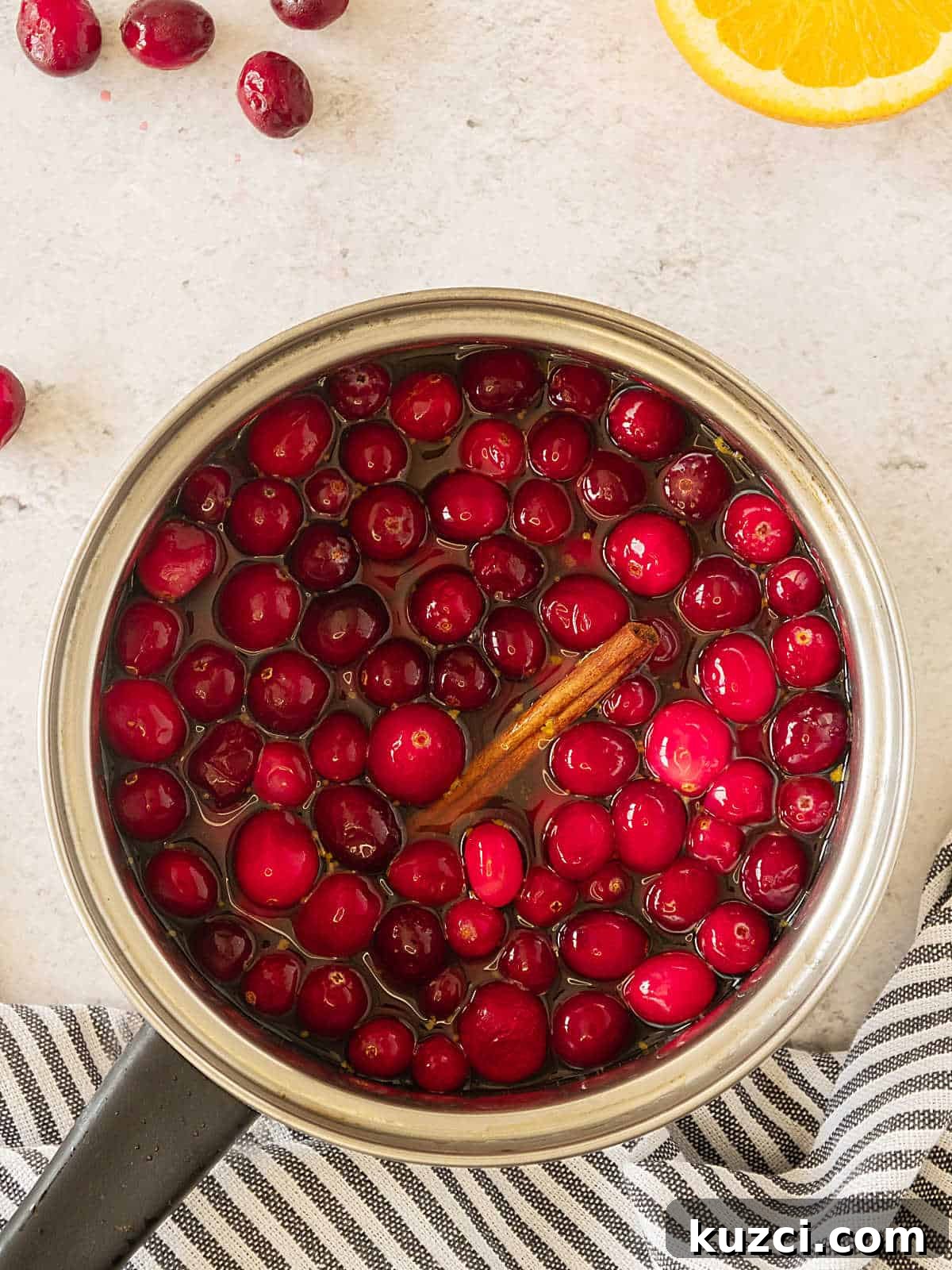 Homemade Cranberry Orange Sauce with Fresh Orange Juice 5 Metal saucepan with cranberries before cooking. Beige surface, striped cloth.