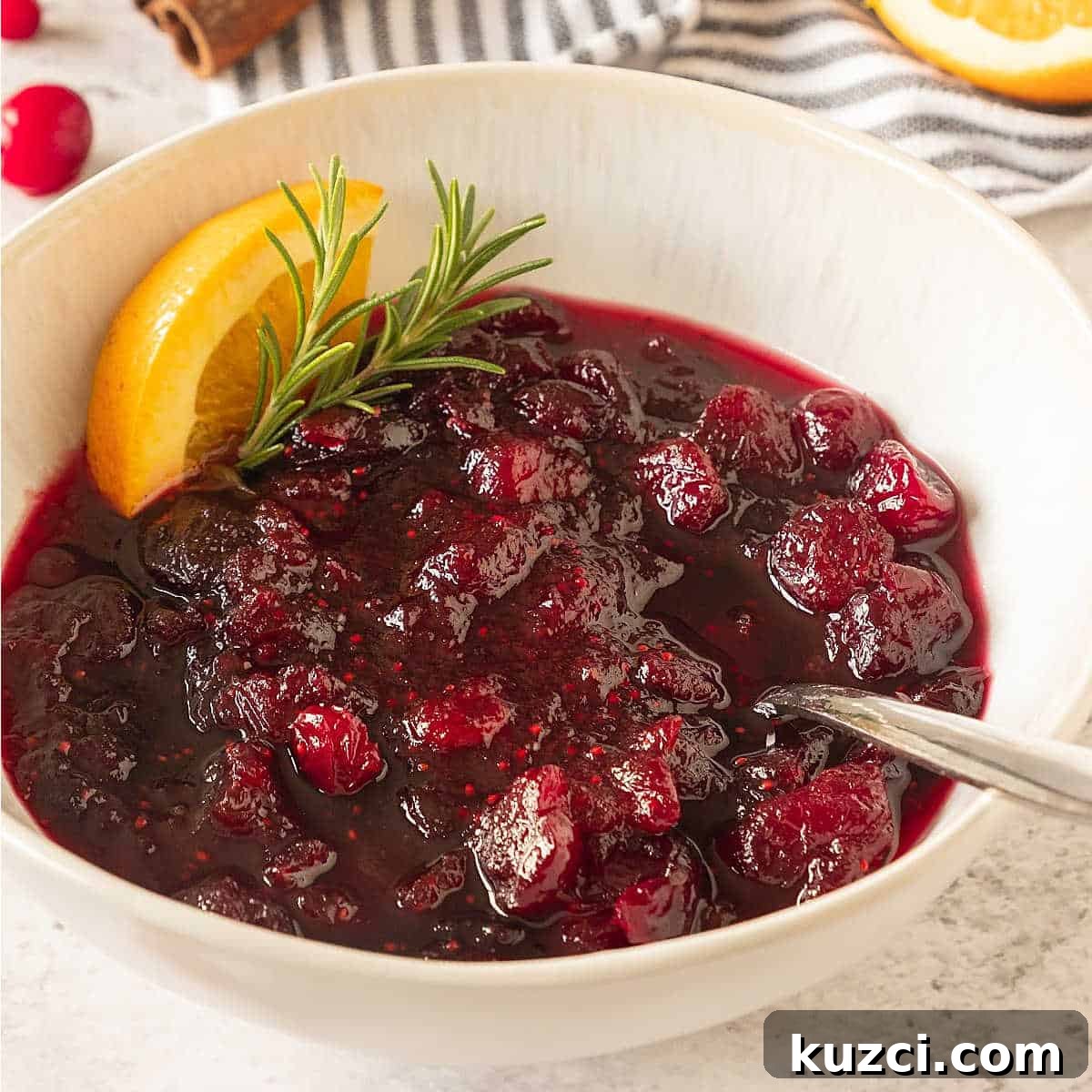Homemade Cranberry Orange Sauce with Fresh Orange Juice 6 Orange cranberry sauce in a white bowl with a spoon, rosemary sprig and orange wedge.