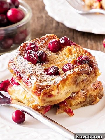 Serving of cranberry French toast on a white plate. Silver fork. Wooden surface.