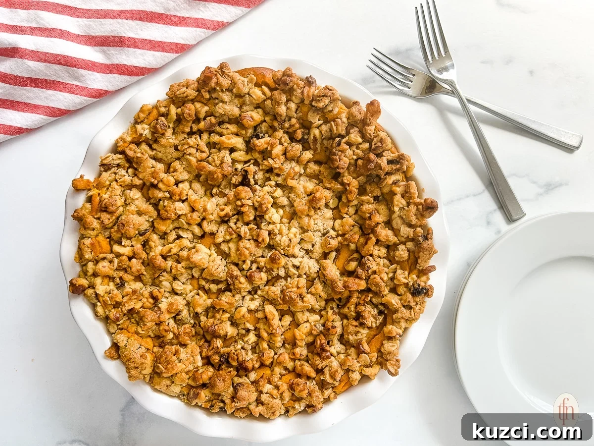 A whole pie with crumble on top next to an empty plate and two crossed forks on a white background.