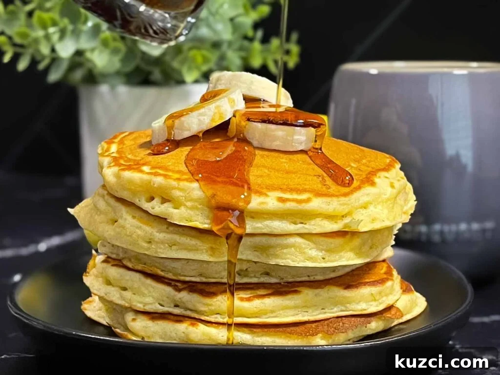 Fluffy Homemade Buttermilk Banana Pancakes 2 Fluffy banana pancakes stacked high with golden edges and soft centers, served with syrup and sliced bananas.