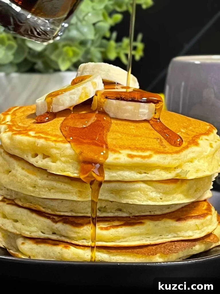 Fluffy Homemade Buttermilk Banana Pancakes 11 Fluffy banana pancakes stacked high with golden edges and soft centers, drizzled with maple syrup.