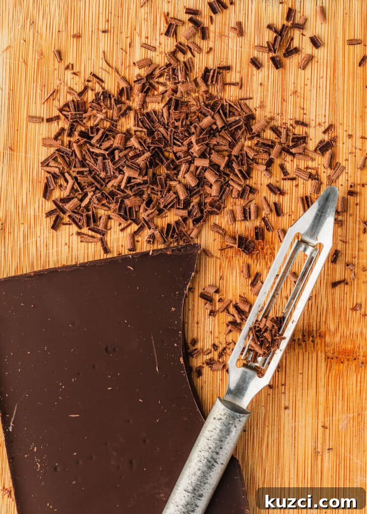 Mini Easter Egg Cheesecakes with Chocolate Ganache Recipe 13 A bar of chocolate, vegetable peeler, and chocolate shavings on a wood board.
