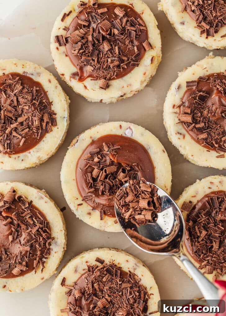 Mini Easter Egg Cheesecakes with Chocolate Ganache Recipe 17 A hand using a spoon to top mini egg cheesecakes with chocolate curls.