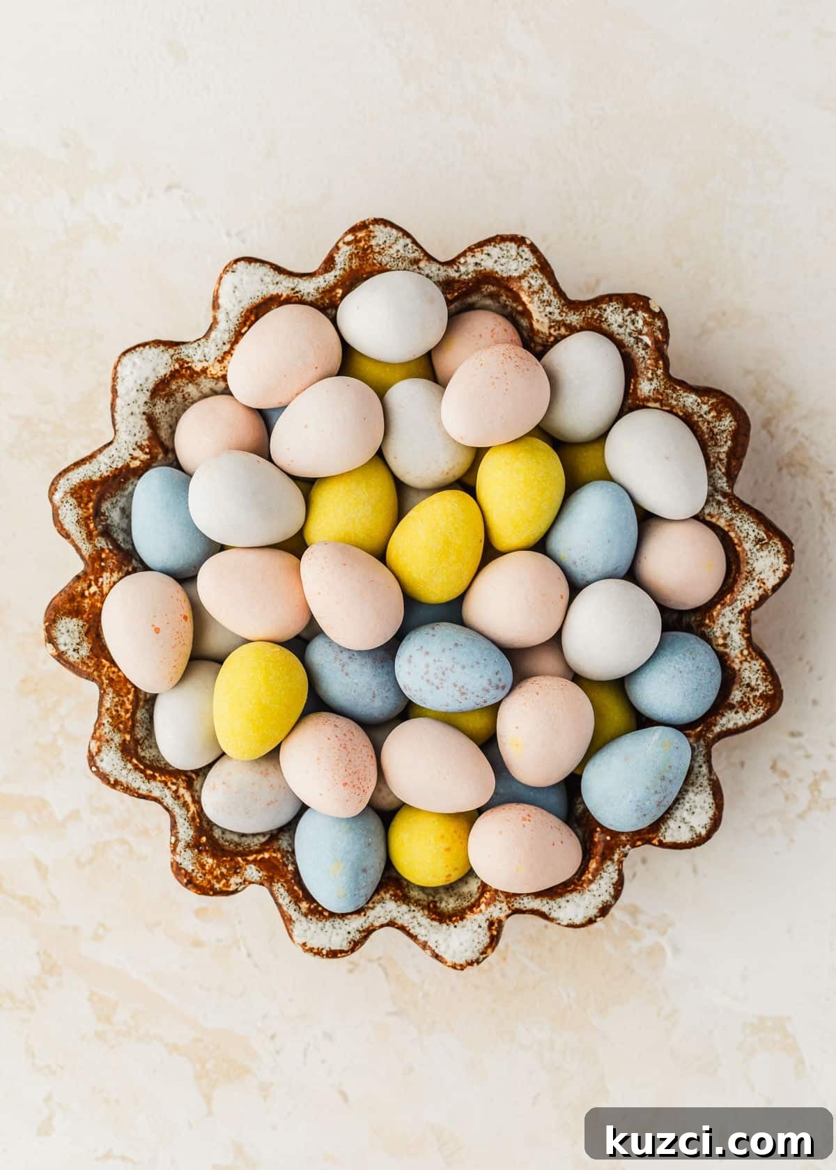 Mini Easter Egg Cheesecakes with Chocolate Ganache Recipe 3 A brown and white bowl of egg candies on a beige counter.