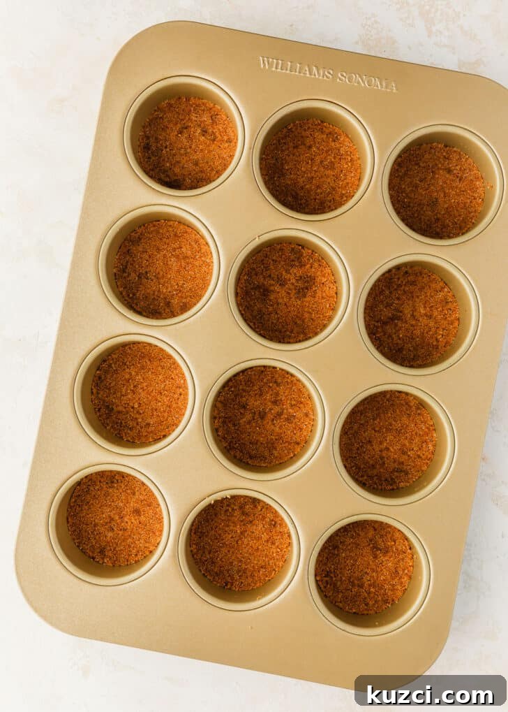 Mini Easter Egg Cheesecakes with Chocolate Ganache Recipe 6 A mini cheesecake pan with graham cracker crusts on a tan counter.