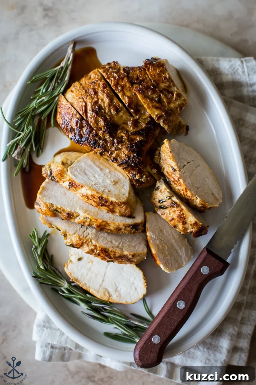 Overhead photo of a sliced turkey tenderloin on an oval plate with two sprigs of rosemary and a sharp knife