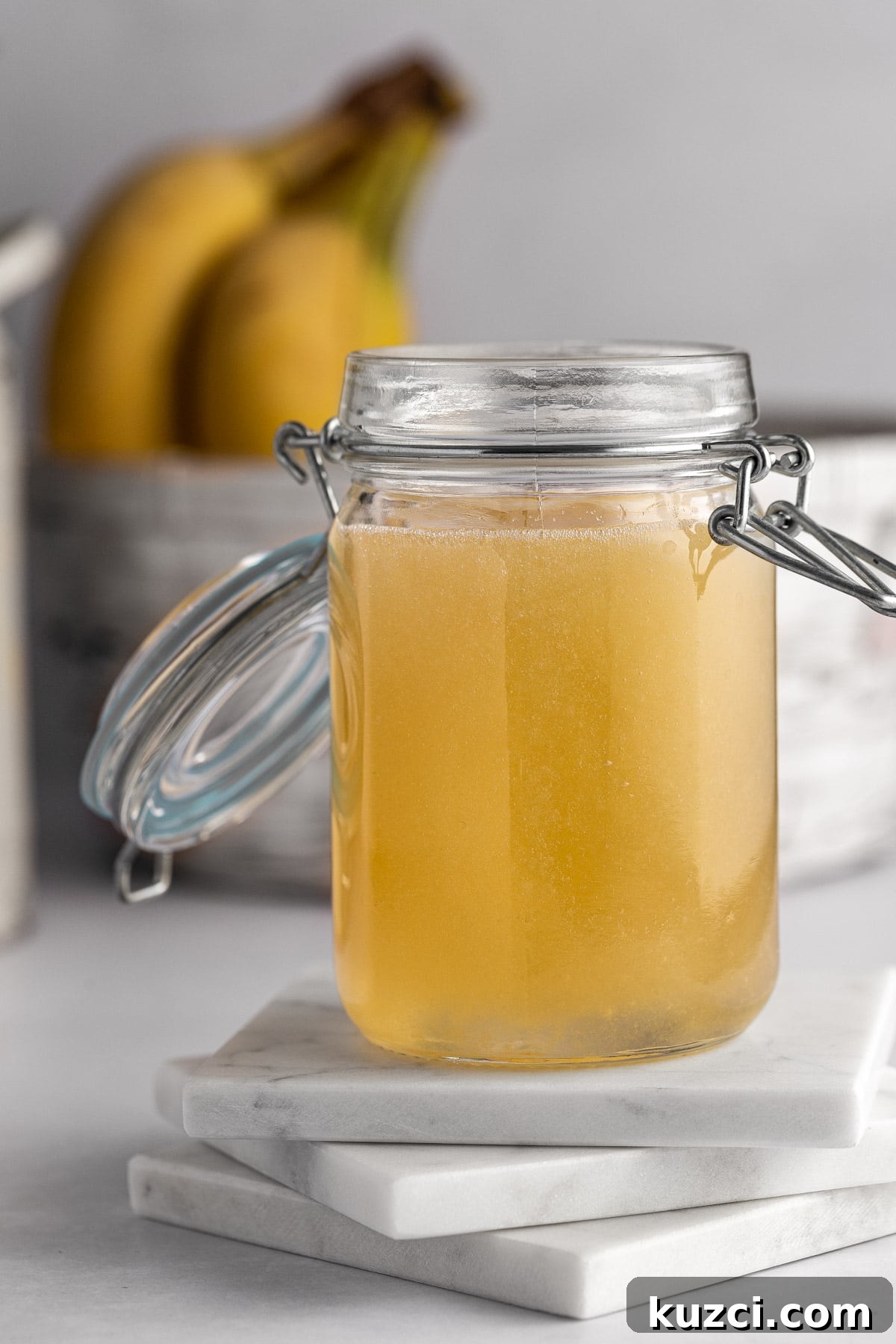 Homemade Banana Syrup for Pancakes, Cocktails and Desserts 7 A jar of banana simple syrup sitting on three square white marble coasters.