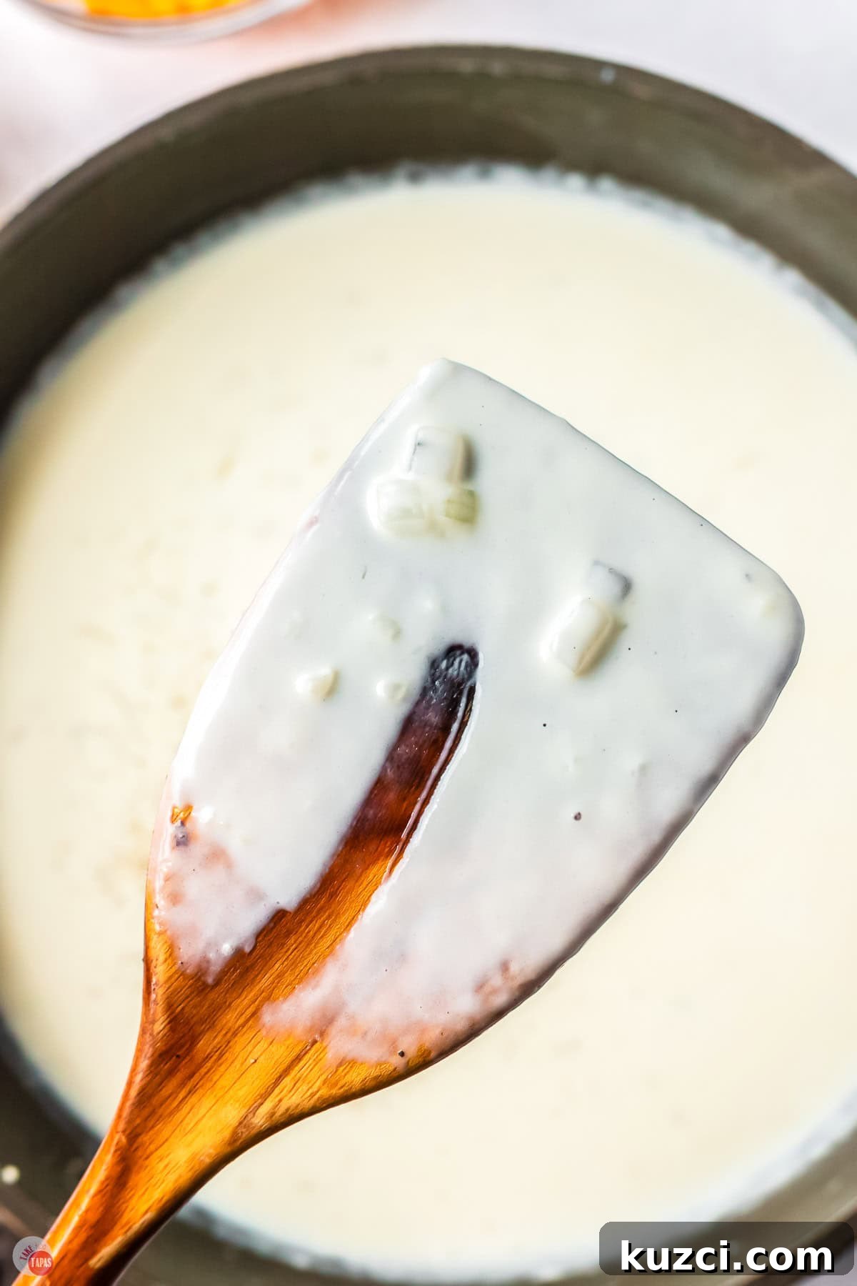 close up of cream sauce on a wood spoon with a finger swipe missing out of it