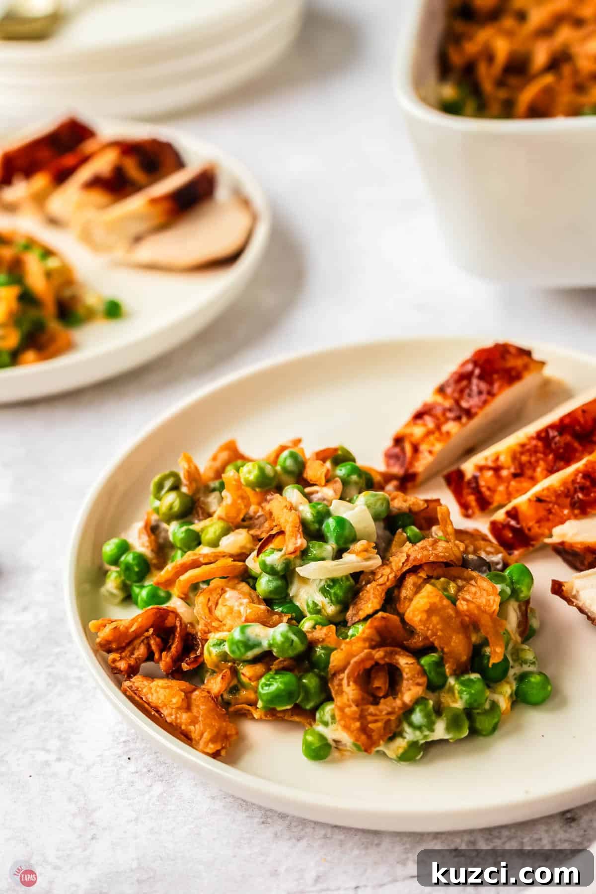 white plate with sliced chicken breast and green peas next to it