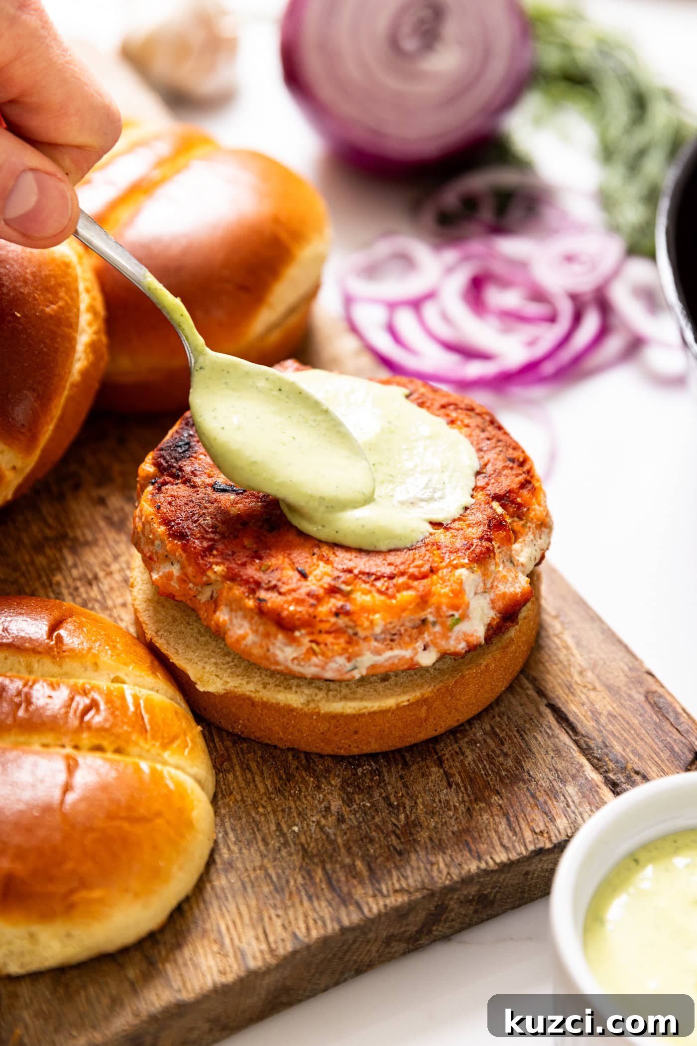 Creamy Dill Aioli Recipe: Garlic and Herb Sauce 3 Spoon putting dill aioli sauce on top of salmon burger sitting on a golden bun.