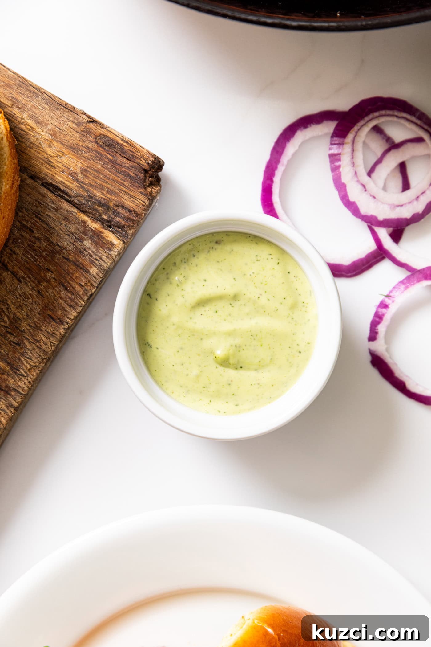 Creamy Dill Aioli Recipe: Garlic and Herb Sauce 4 White bowl filled with dill aioli with wooden cutting board and red onions.