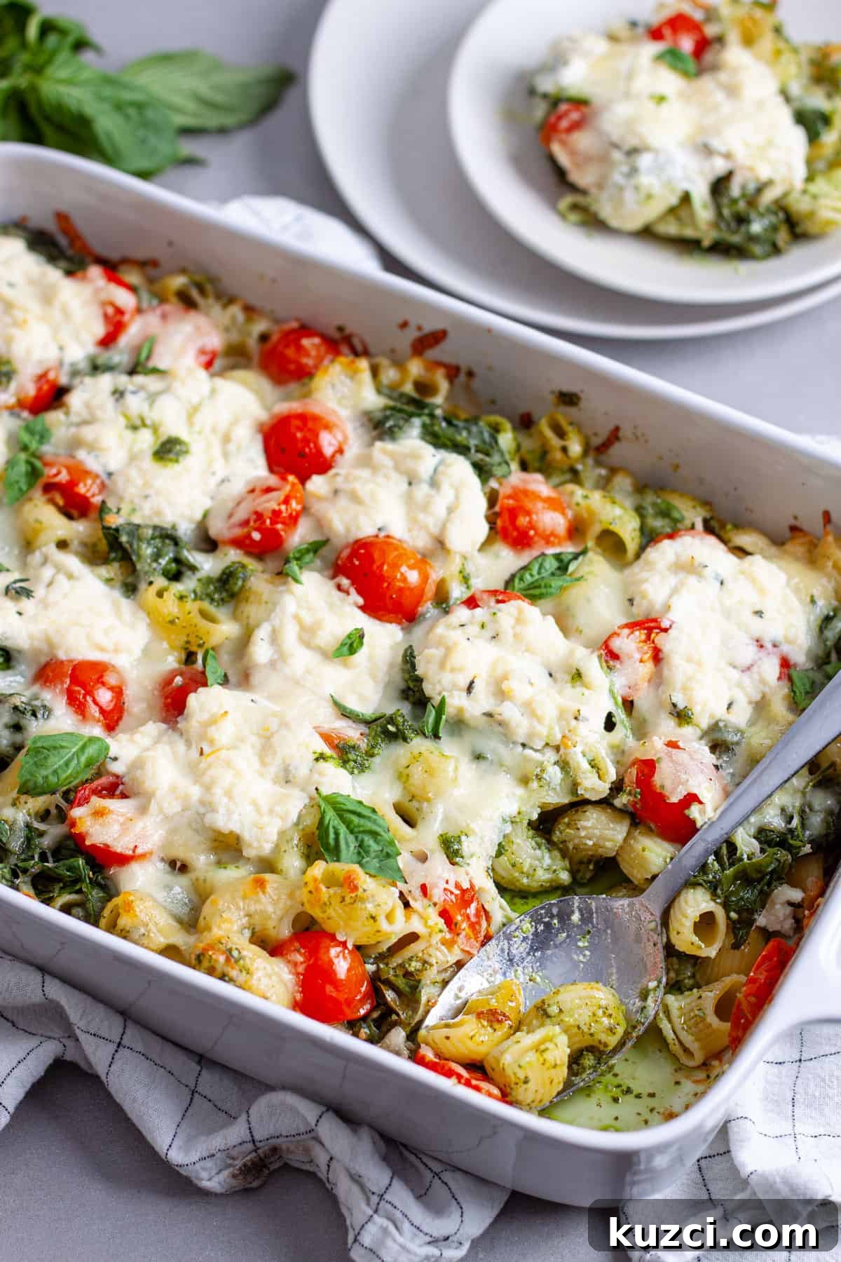 A spoon taking a serving of ricotta pesto pasta out of a white casserole dish.