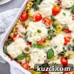 A close up of a baked ricotta pesto pasta topped with tomatoes, spinach and melty cheese.