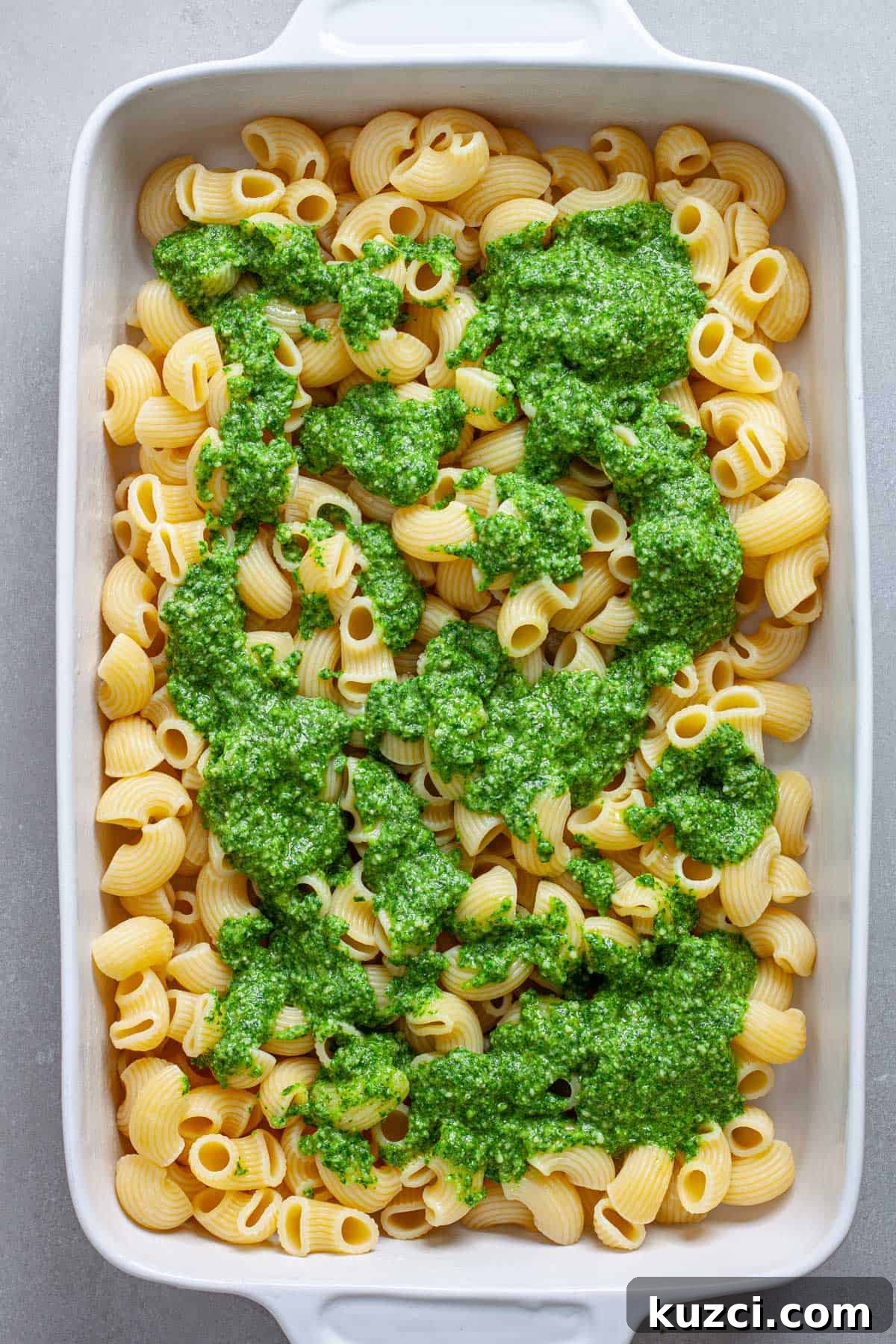 A casserole dish of cooked pasta with pesto spooned on top.