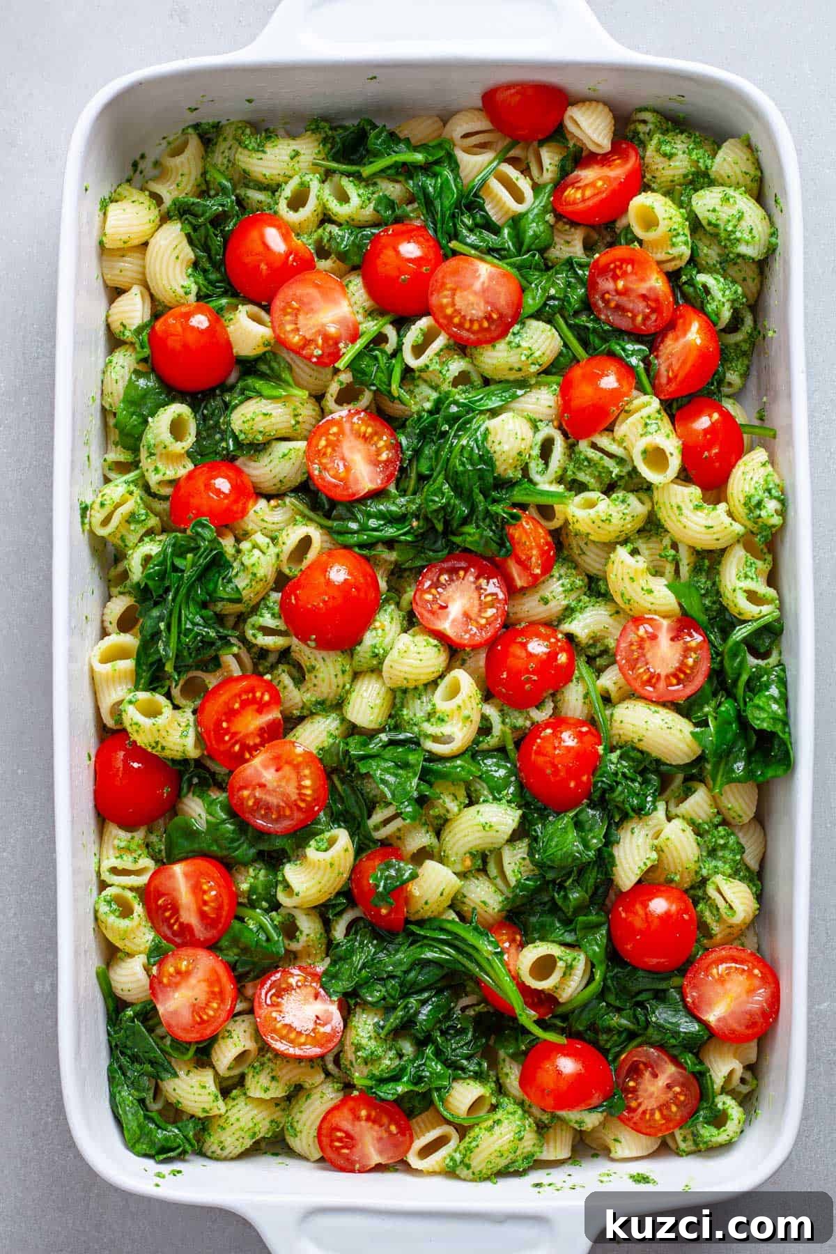 Cherry tomatoes and wilted spinach on top of a casserole dish of pasta and pesto.