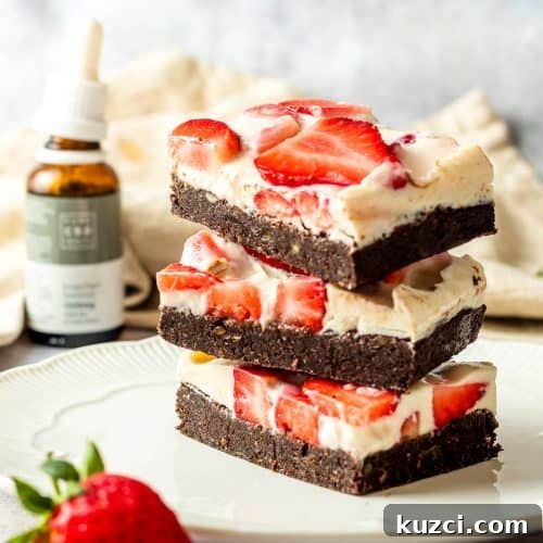 No-Bake Cheesecake Brownies Recipe 5 Three cheesecake brownies with strawberries stacked on top of each other on a white plate. There is a strawberry as a prop and a bottle of CBD oil in the background.