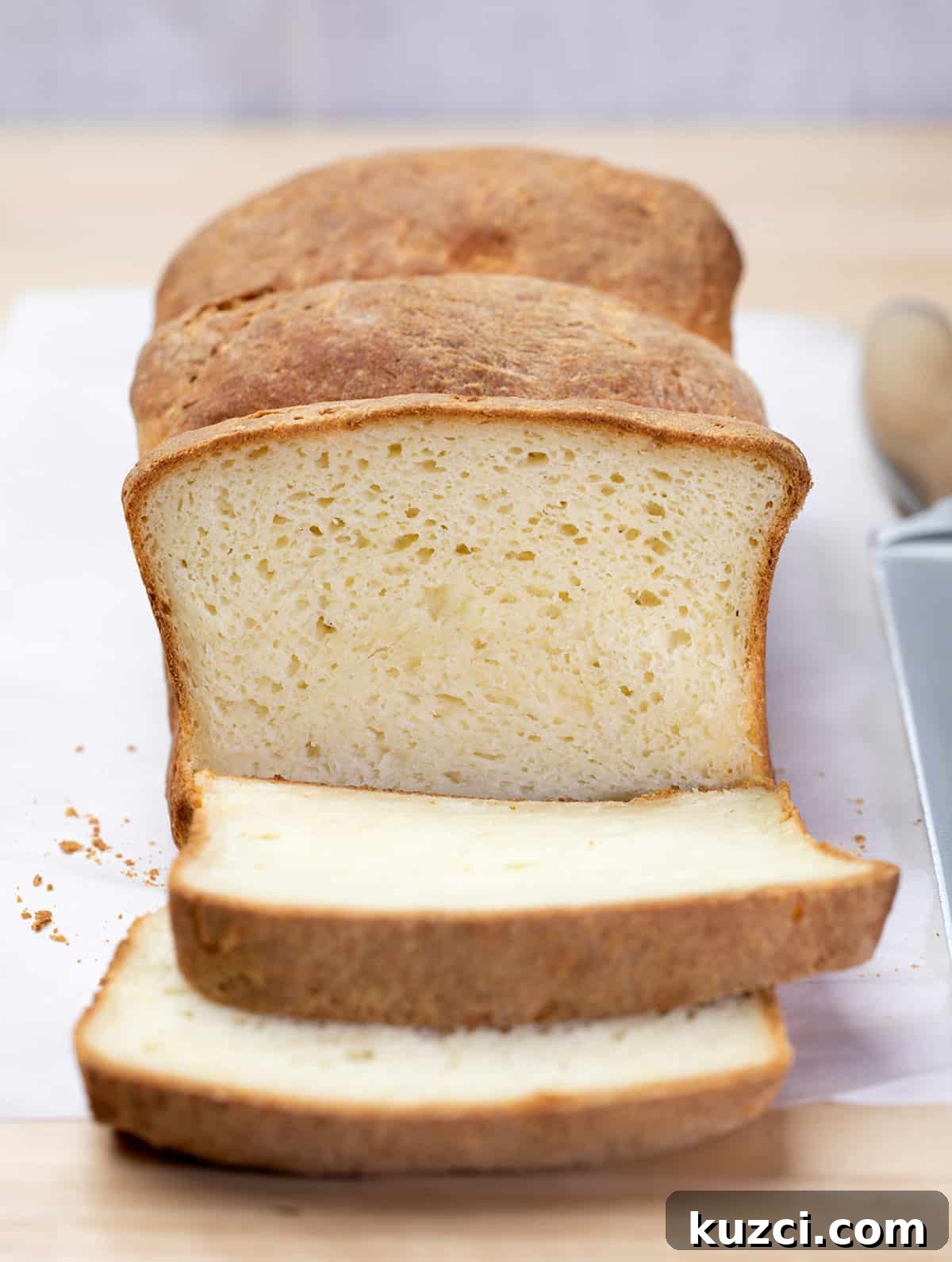 Loaf of bread with 2 slices on white paper with a large bread knife