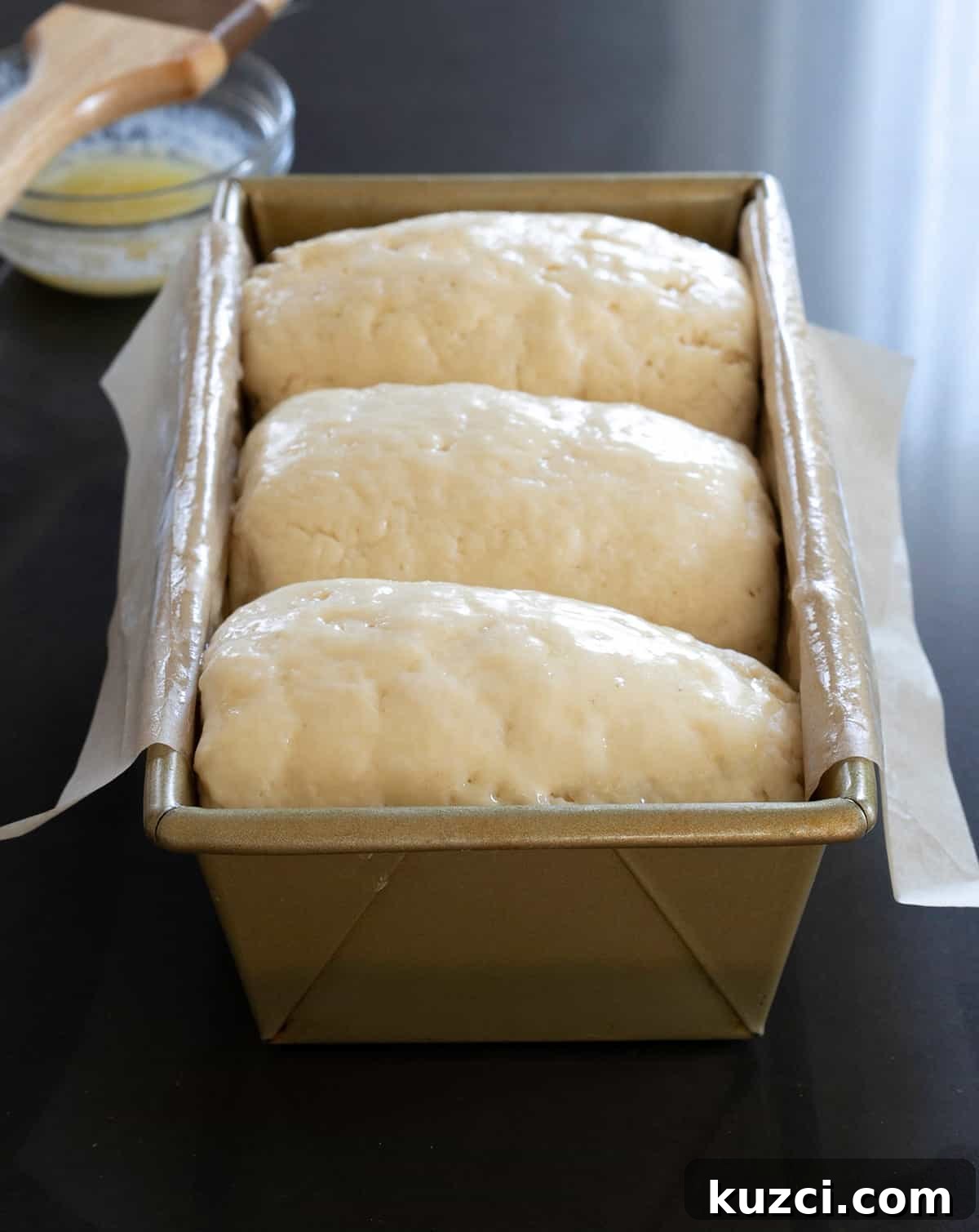 A loaf pan with white paper lining and three pieces of raw bread dough