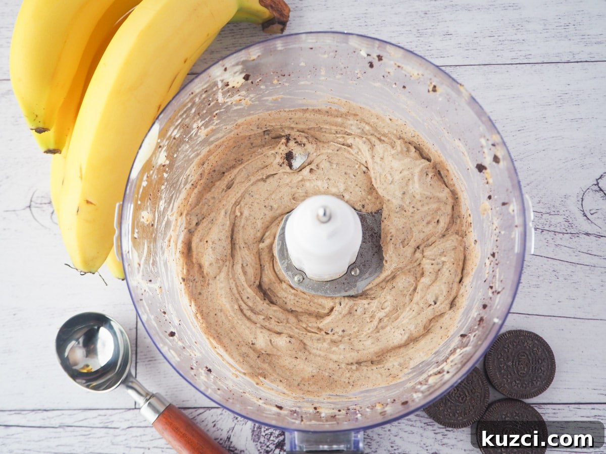 Cookies and Cream Nice Cream Recipe 12 Top down view of open food processor with cookies and cream nice cream, with bananas, Oreos and ice cream scoop on the side.