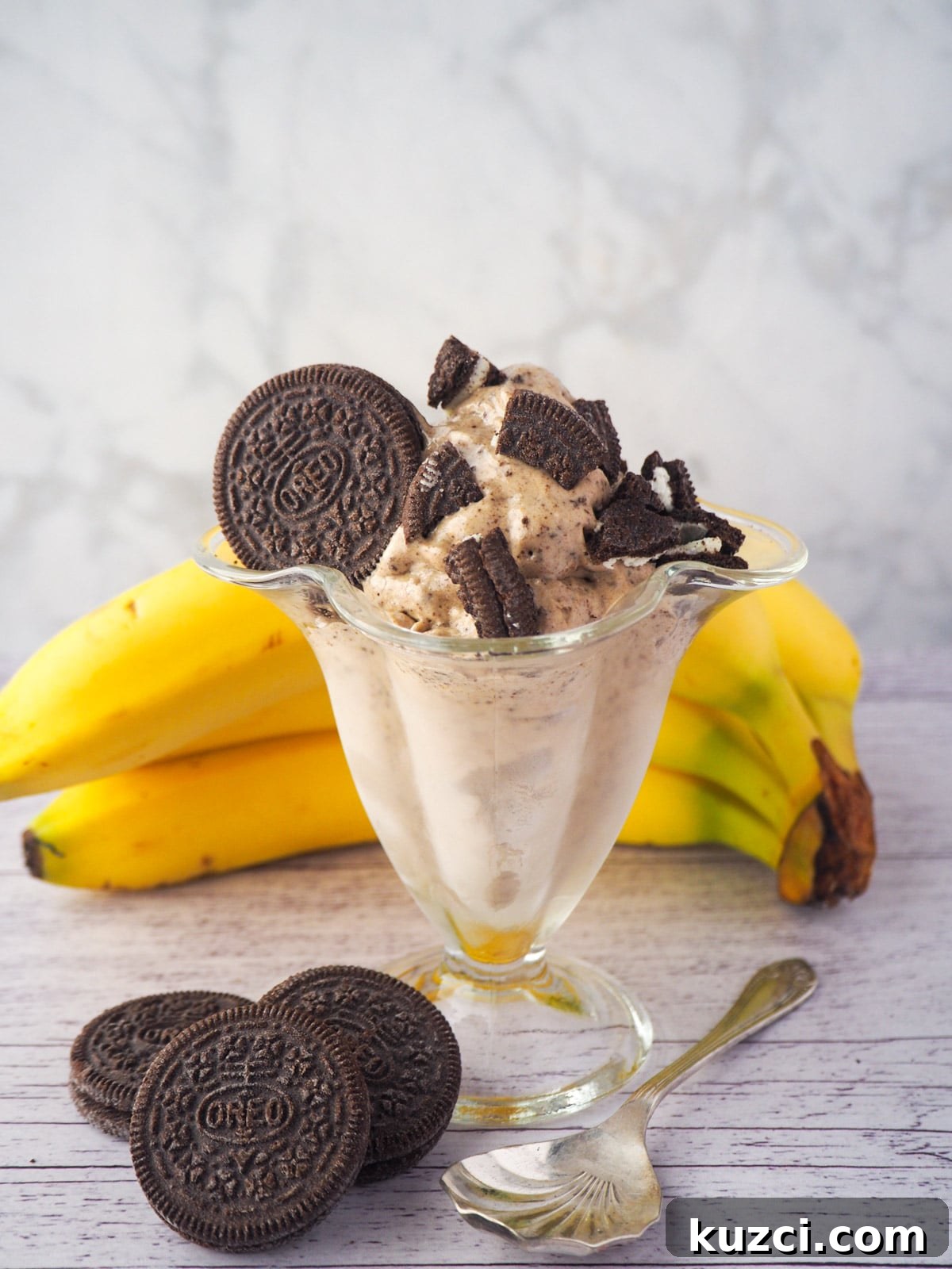 Cookies and Cream Nice Cream Recipe 16 Serve of cookies and cream nice cream in a sundae glass, with pieces of Oreos, bananas and whole Oreos in the background.