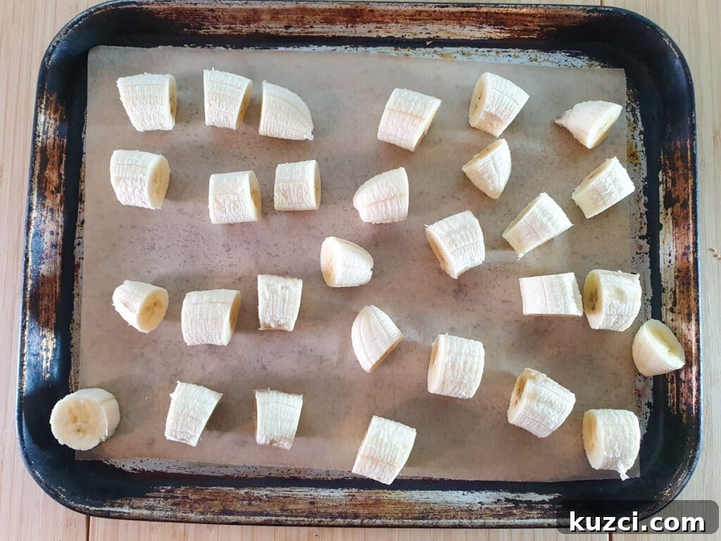 Cookies and Cream Nice Cream Recipe 5 Laying out sliced bananas on a baking tray lined with baking paper, with pieces not touching each other.