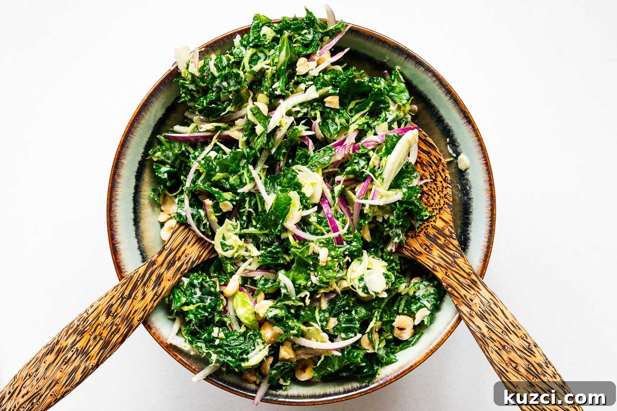 Tossing kale salad with a creamy tahini dressing using a pair of wooden salad tongs.