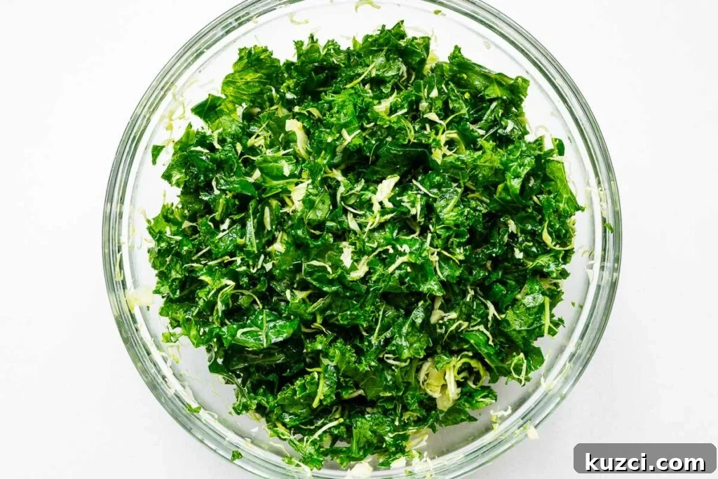 A large bowl of raw kale leaves massaged with olive oil and salt to soften.