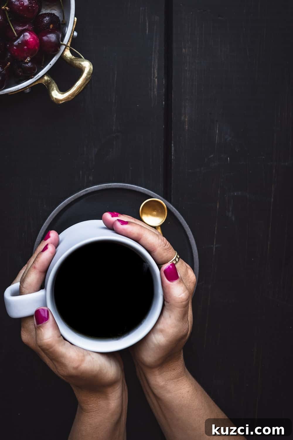 My pink nails holding a cup of black coffee, with a bowl of cherries in the corner.