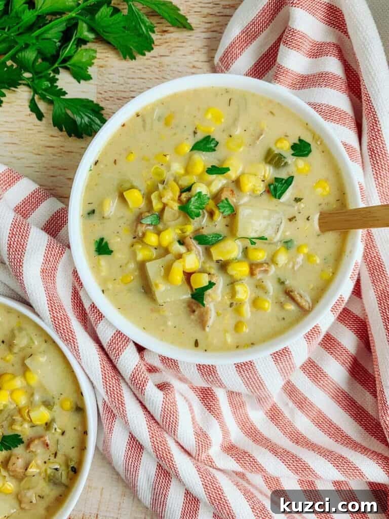 A bowl of corn chowder with a wooden spoon in the bowl. Red striped towel under the bowl of chowder