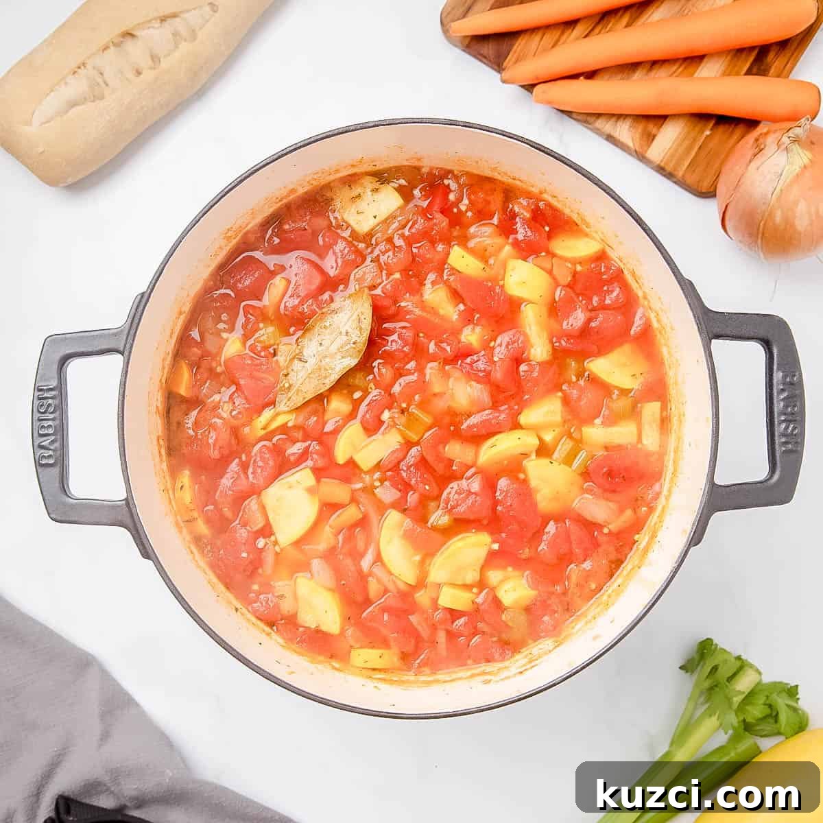 Pot of vegetable soup with tomatoes and squash on a stovetop, surrounded by bread, carrots, onion, celery, and a napkin.