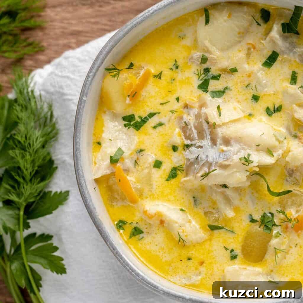 A bowl of fish chowder with green herbs along the side