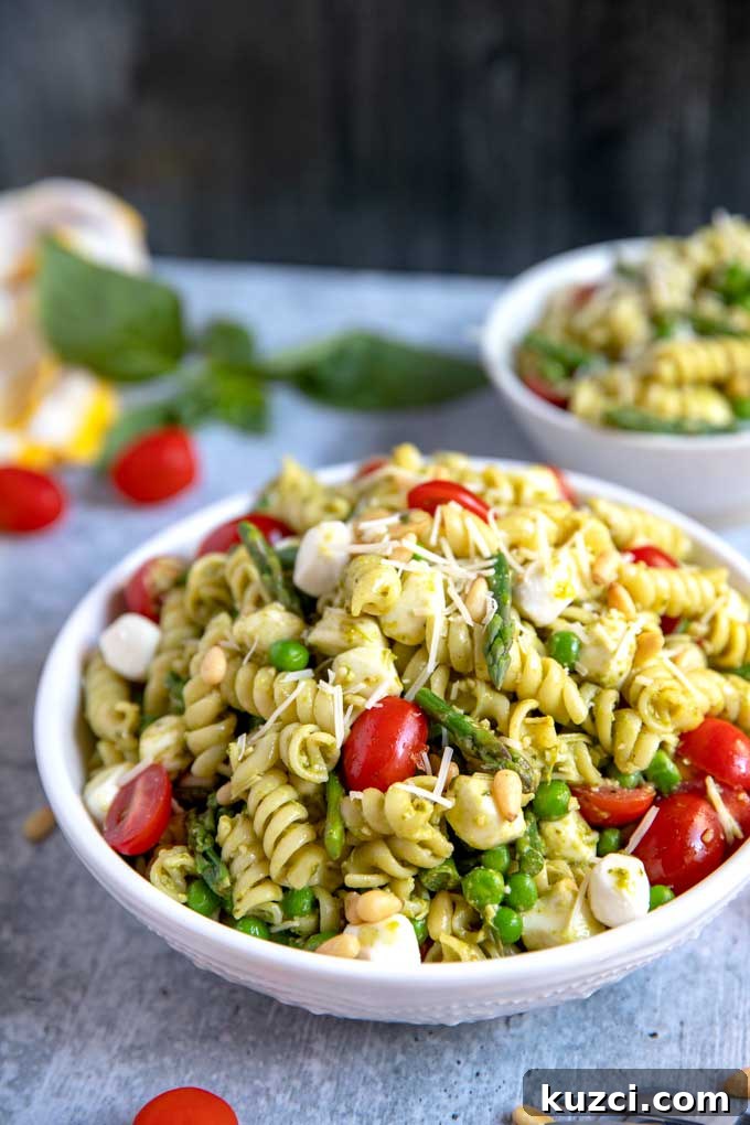 A white bowl filled with Pesto Pasta Salad with asparagus, peas, mozzarella tomatoes and Parmesan