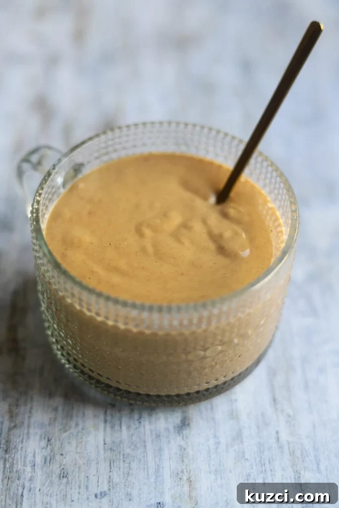 Peanut Lime Dressing Recipe 2 A glass bowl of peanut lime salad dressing made with soy sauce, sweet chili sauce, and rice vinegar along with smooth peanut butter, sits on a gray background.
