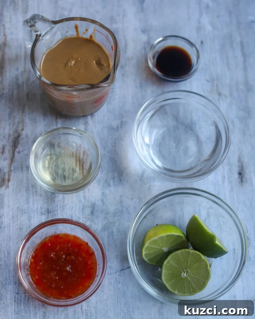 Peanut Lime Dressing Recipe 4 overhead view of several glass bowls of various sizes holding ingredients for peanut dressing like fresh cut limes, rice vinegar, red sweet chili sauce, water, soy sauce and a glass measuring cup full of smooth peanut butter all sit on a gray surface.
