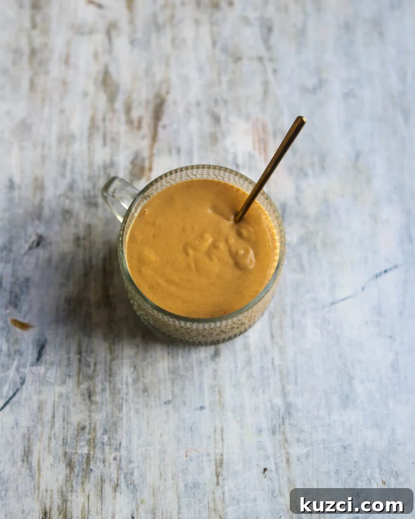 Peanut Lime Dressing Recipe 5 overhead view of a round glass dish containing vegan lime peanut salad dressing made with rice vinegar, fresh lime juice, sweet chili sauce, soy sauce and smooth peanut butter sits on a gray marble background.