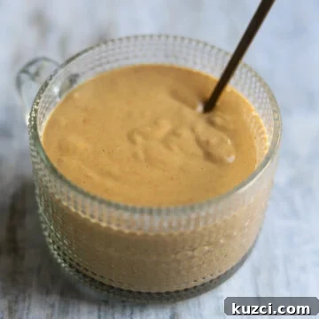 Peanut Lime Dressing Recipe 8 A glass bowl of peanut lime salad dressing made with soy sauce, sweet chili sauce, and rice vinegar along with smooth peanut butter, sits on a gray background