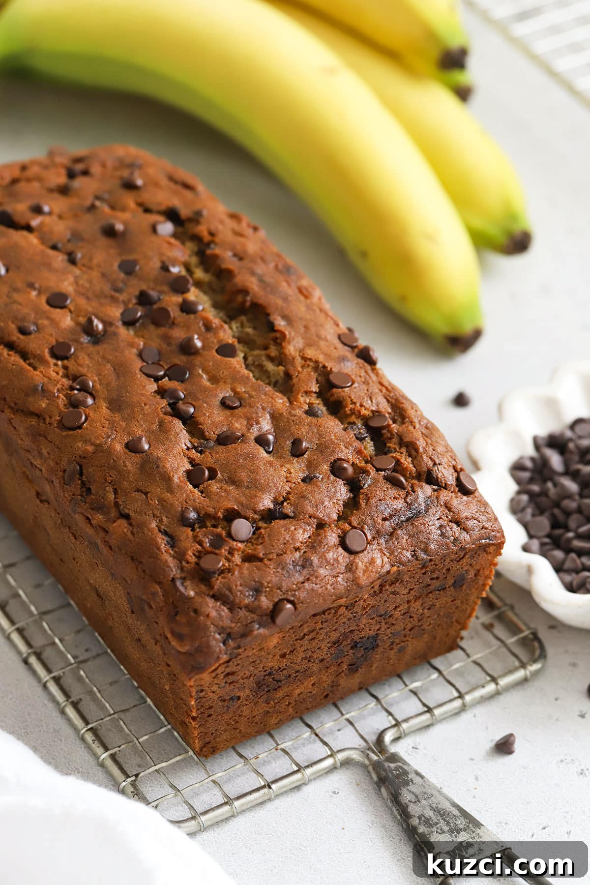 a loaf of gluten-free chocolate chip banana bread with chocolate chips and bananas in the background